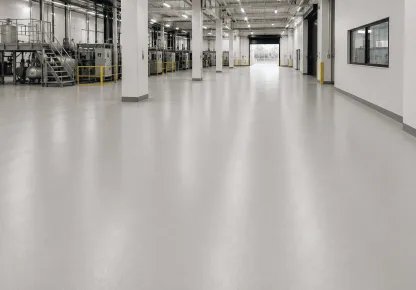 Piso monolítico contínuo e uniforme em um amplo ambiente industrial, com acabamento liso e equipamentos ao fundo.
